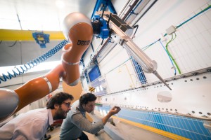 José Navarro, IDPSA, und José Saenz vom Fraunhofer IFF prüfen, wie VALERI das Dichtmittel auf ein Flugzeugbauteil aufgebracht hat. (Foto: KUKA)